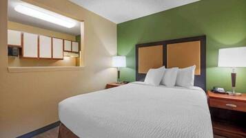 A hotel room with a large bed, two bedside tables, a nightstand, a mirror, and a green accent wall.