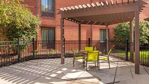 Un patio cubierto con pérgola, un edificio de ladrillo y un jardín cercado.