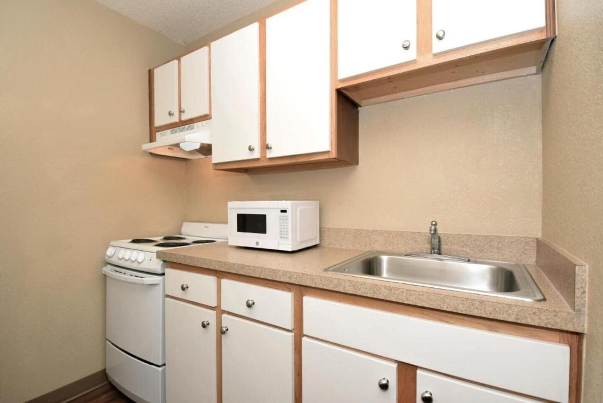 A kitchen with white cabinets, a microwave, a stove, and a sink.