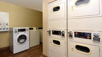 A laundry room with multiple washing machines and dryers, a whiteboard with safety instructions, and a wooden floor.