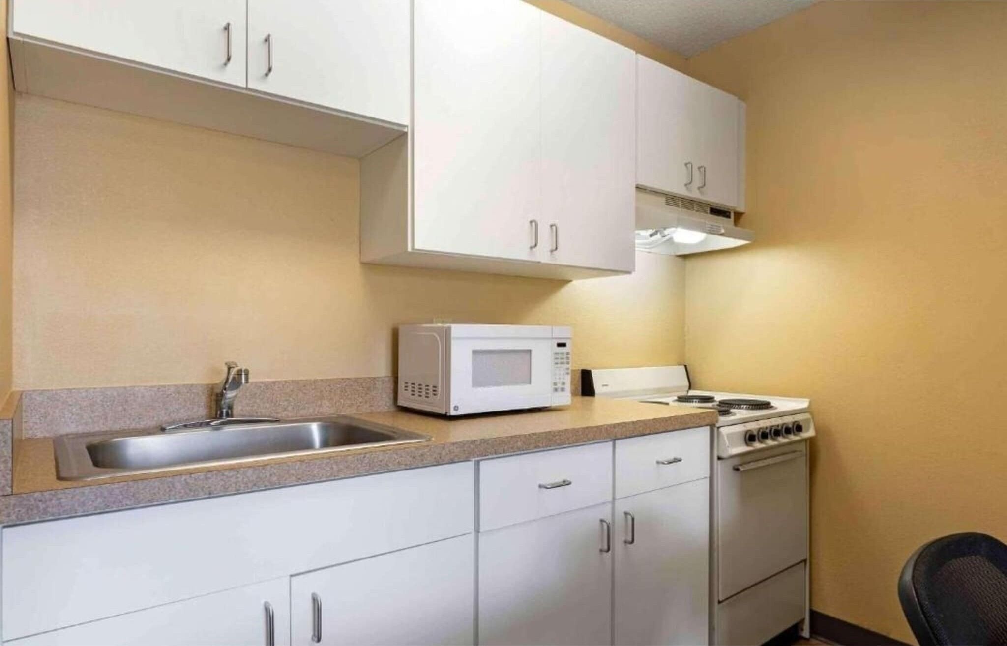 A compact kitchen with white cabinets, a microwave, a stove, and a sink.