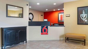 Un espace d’accueil d’hôtel avec un comptoir noir, une horloge, un banc et un mur d’accent rouge.