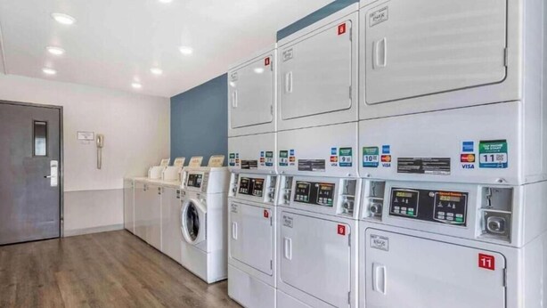 A row of white laundry machines with numbered doors, a washing machine, and a door with a handle.