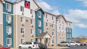 A multi-story hotel with a prominent '6' sign, a parking lot, and a small entrance building.