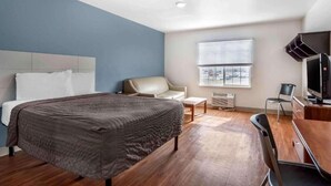 A hotel room with a bed, a chair, a desk with a computer, and a TV.