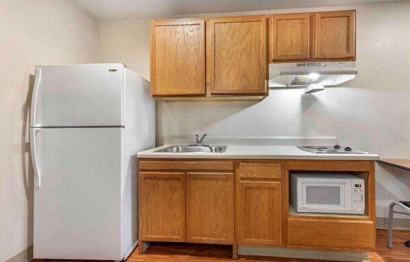 A compact kitchen with wooden cabinets, a white refrigerator, a sink, a stove, and a microwave.