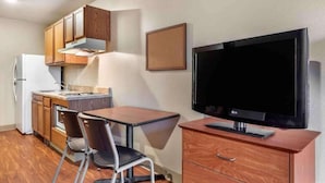 A compact kitchenette with a refrigerator, stove, and wooden cabinets. A flat-screen TV is mounted on the wall above a wooden cabinet. - 1 Full Bed | ADA/Tub/Non-Smoking/Kitchen (Shreveport LA)