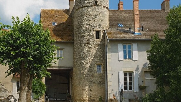 Een stenen toren verbonden met een gebouw, met een grindpad en een boom op de voorgrond.