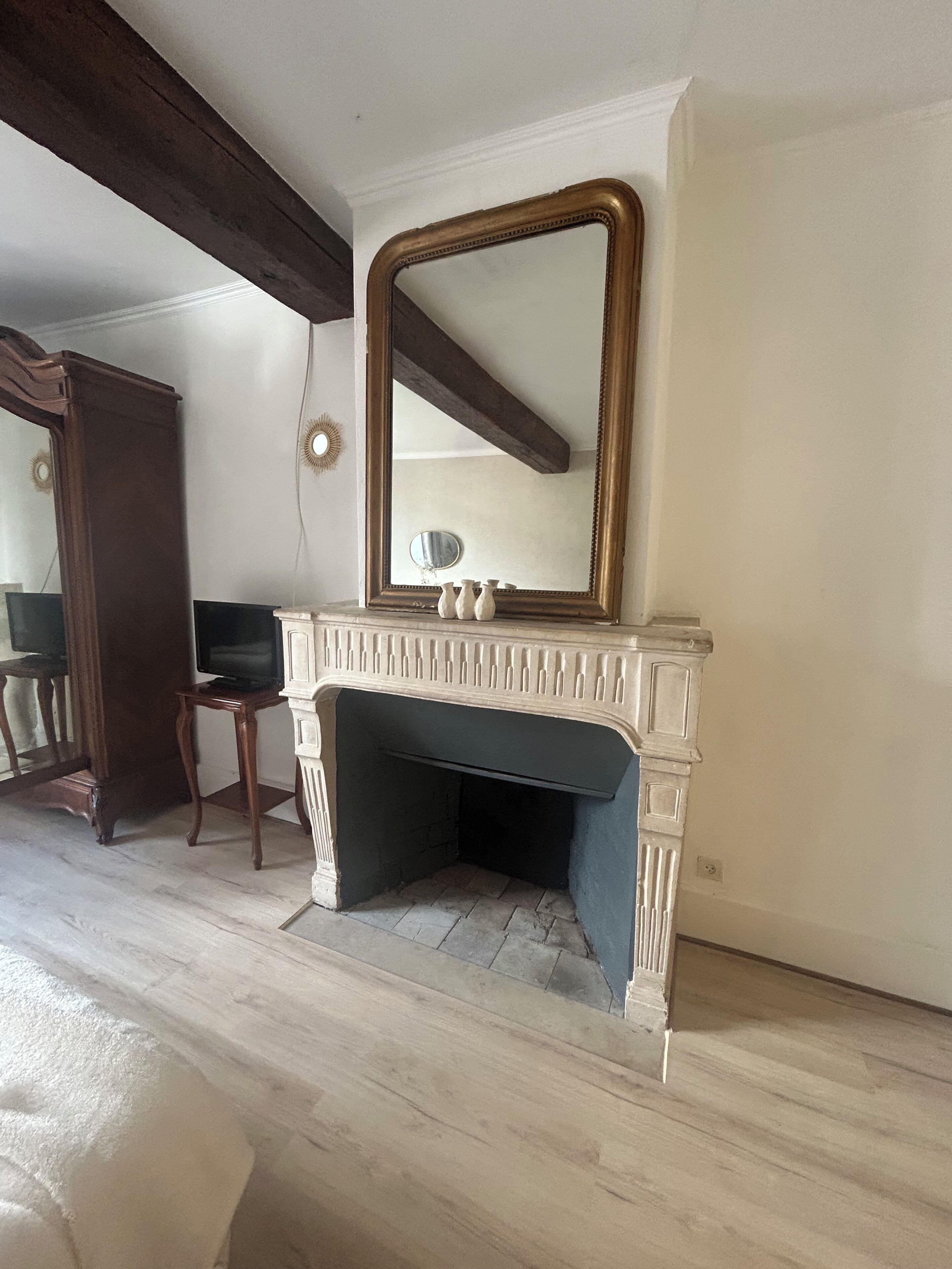 A room with a fireplace, a mirror, and a television on a stand.