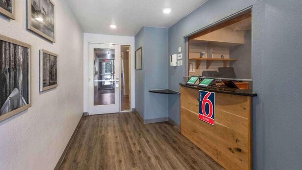 Zona de recepción de un hotel con un mostrador de madera, cuadros enmarcados en la pared y una puerta que da a una habitación.