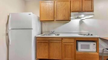 A compact kitchen with wooden cabinets, a white refrigerator, a sink, a stove, and a microwave.