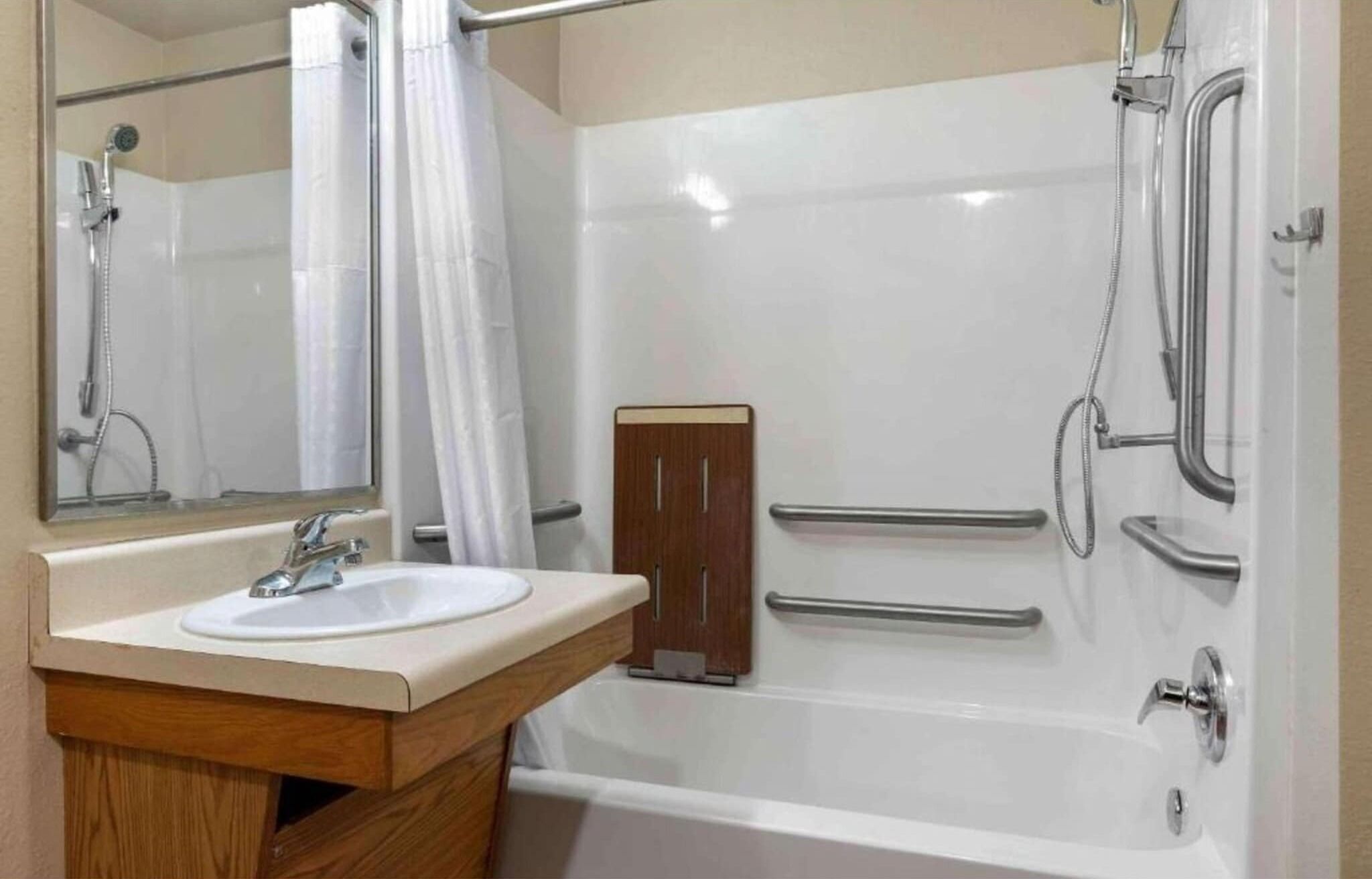 A bathroom with a white sink, a mirror, a shower with a handheld showerhead, and a wooden cabinet.