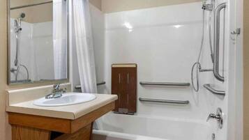 A bathroom with a white sink, a mirror, a shower with a handheld showerhead, and a wooden cabinet.