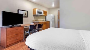 Un dormitorio con una cama, un escritorio con televisor, un microondas y un refrigerador.