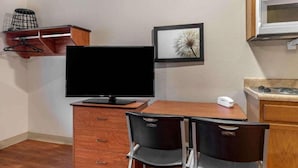 Una pequeña kitchenette con microondas, un televisor de pantalla plana, una mesita, dos sillas y un cuadro en la pared.