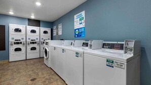 A laundry facility with multiple washing machines and dryers, a control panel, and a poster on the wall. - 1 Full Bed | Non-Smoking, Kitchen (Shreveport LA)