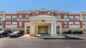 Een hotel met meerdere verdiepingen, een centrale ingang, nummer 201, en een parkeerplaats met diverse auto's.