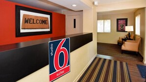Een hotel receptie met een 'WELCOME' bord, een bord met '6 suites', een receptiebalie, een deur, een lounge met een bank en een lamp.