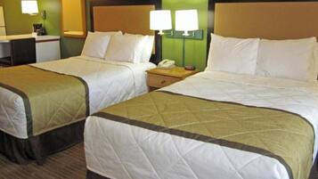 A hotel room with two beds, each with a quilted bedspread and pillows, a bedside table with a lamp, and a desk with a telephone.