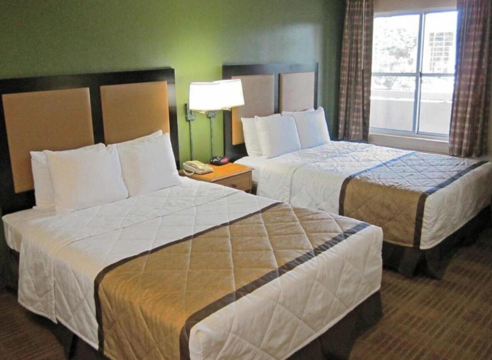 Two double beds with headboards, a bedside lamp, and a window with curtains.