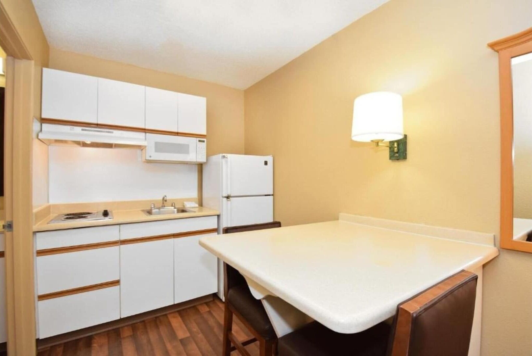 Una cocina compacta con armarios blancos, microondas, refrigerador y una mesa con sillas.