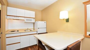 Una cocina compacta con armarios blancos, microondas, refrigerador y una mesa con sillas.