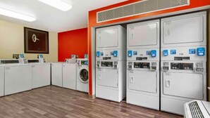 A laundry facility with multiple washing machines and dryers, a wooden floor, and a red accent wall. - 2 Full Beds | Non-Smoking, Kitchen (Germantown)