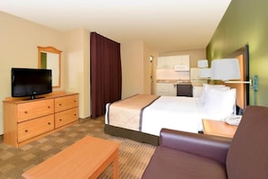 Habitación de hotel con cama, televisor en una cómoda, escritorio, silla y baño a la vista a través de una puerta abierta.