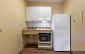 Una kitchenette compacta con gabinetes blancos, un microondas integrado y un refrigerador.