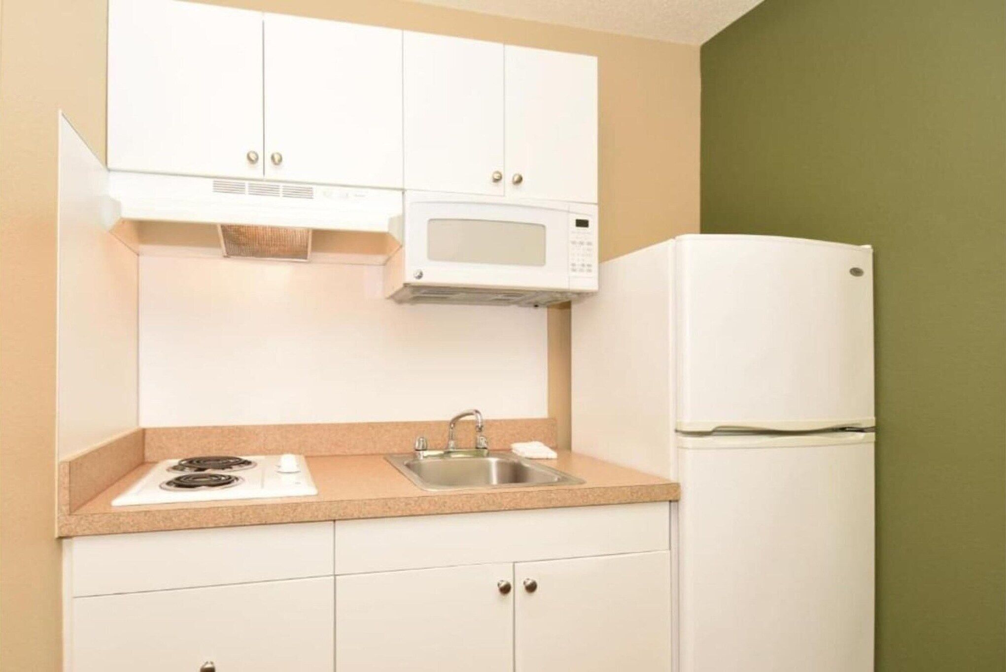 A kitchen with white cabinets, a microwave, a stove, a sink, and a refrigerator.