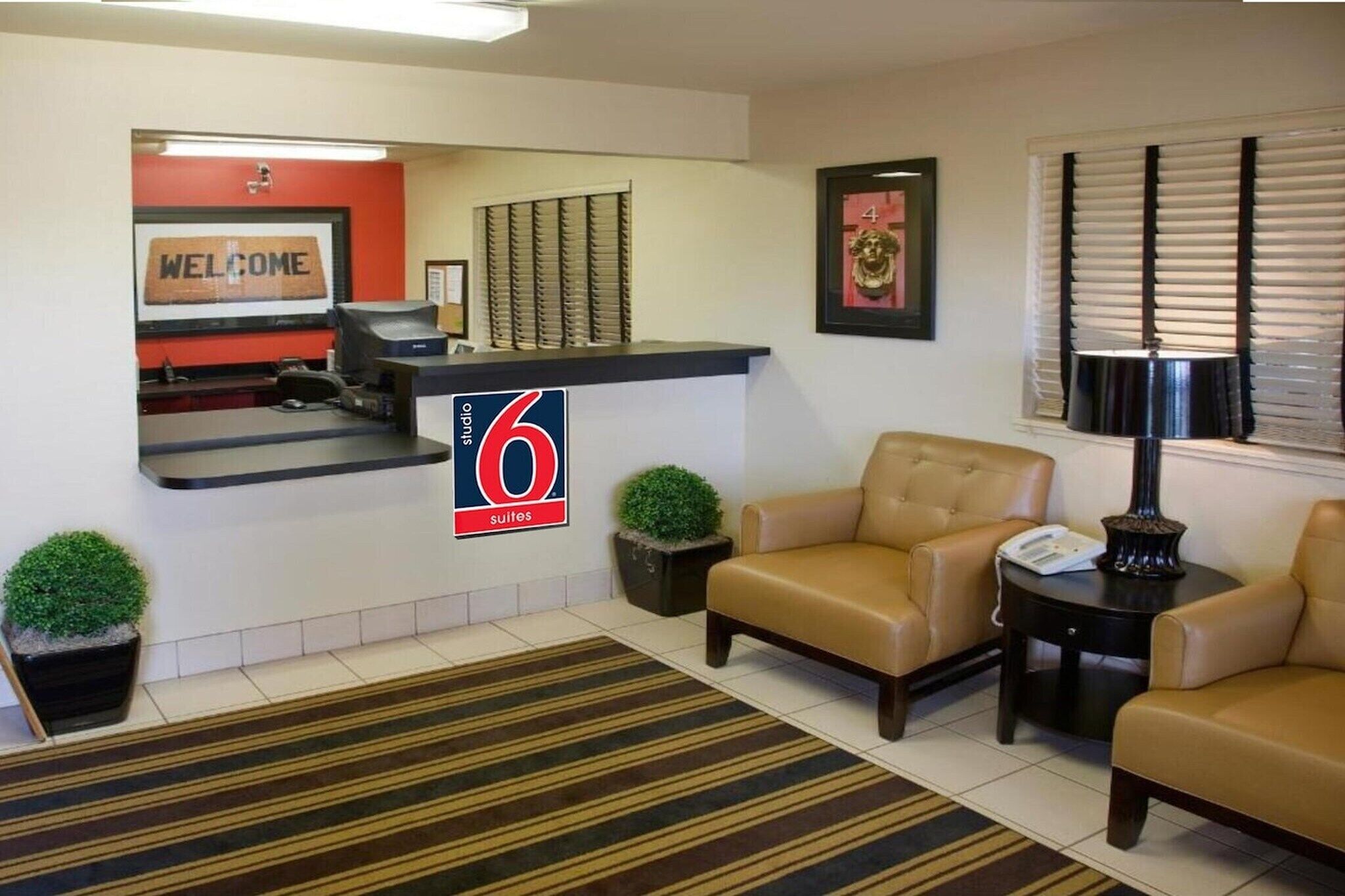 Un hall d'accueil d'hôtel avec une enseigne indiquant « 6 suites », un comptoir de réception, deux canapés, une petite table et un tableau encadré au mur.