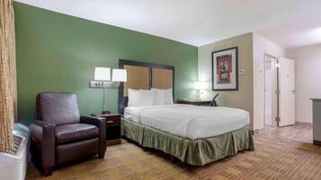 A hotel room with a bed, a chair, a nightstand, a lamp, and a picture on the wall.