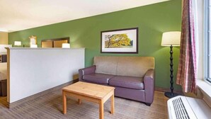 Quarto com sofá, pequena mesa de madeira, luminária e quadro na parede.