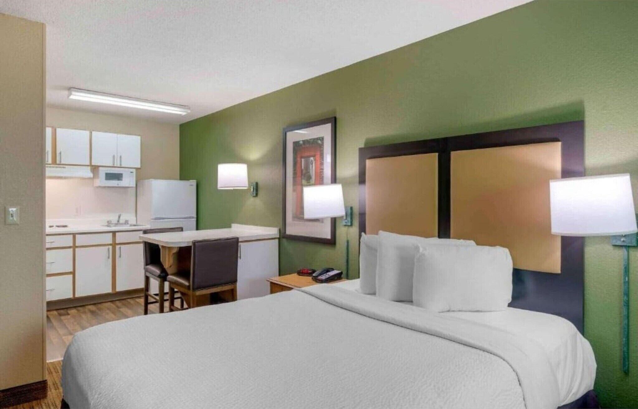 A hotel room with a bed, a desk, a chair, a microwave, and a refrigerator.