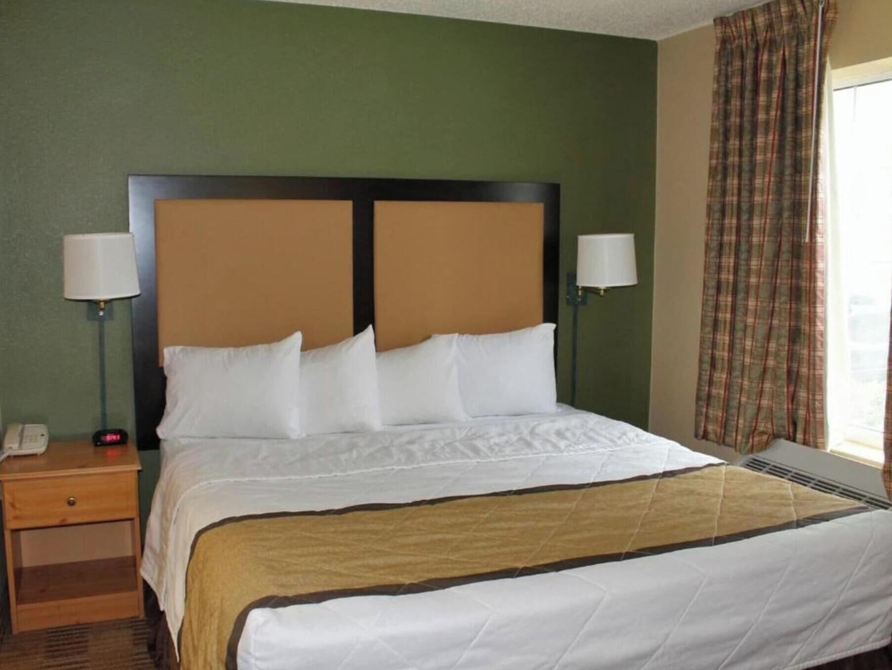 A hotel room with a bed, two bedside lamps, a nightstand, and a window with curtains.