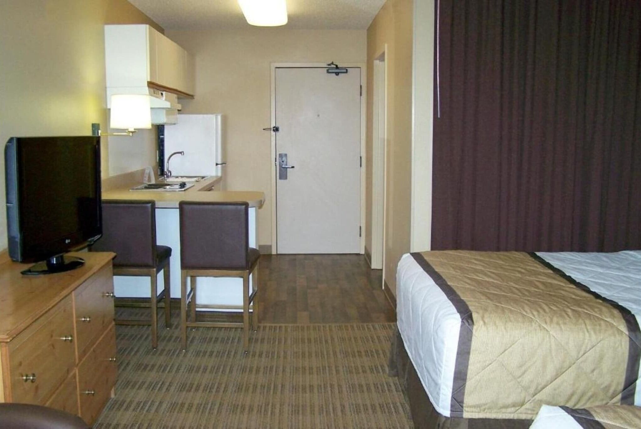 A hotel room with a bed, a television, a desk with a chair, and a door.