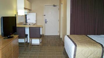 A hotel room with a bed, a television, a desk with a chair, and a door.