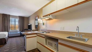 Een compacte hotelkamer met kitchenette, een bed, een televisie en een raam met gordijnen.