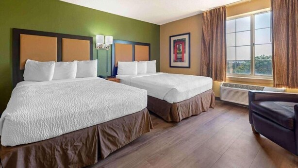 A hotel room with two beds, a window with curtains, a framed picture on the wall, and a chair. - 2 Queen Beds |Non- Smoking, Kitchen (Minneapolis MN)