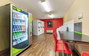 Ein Zimmer mit Getränkeautomaten, einer roten Wand, einer weißen Klimaanlage und einem Tisch mit roten Stühlen.