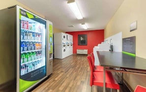 A room with a vending machine, a red wall, a white air conditioning unit, and a table with red chairs. - 1 Queen Bed | ADA/RI Shower/Non-Smoking/Kitchen (Minneapolis MN)