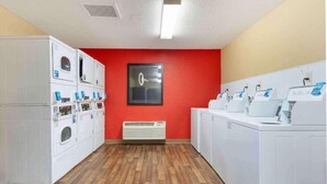 Un cuarto de lavandería con varias lavadoras, un equipo de aire acondicionado central y una pared de acento en rojo.