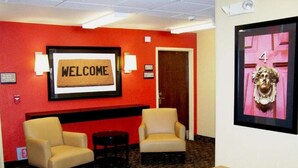 A lobby with a red wall, a welcome sign, two armchairs, a bench, and a framed artwork. - 1 King Bed | Non-Smoking, Kitchen, Shower (Minneapolis MN)