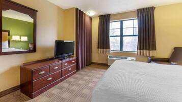 A hotel room with a bed, a TV on a wooden dresser, a window with curtains, and a mirror on the wall.