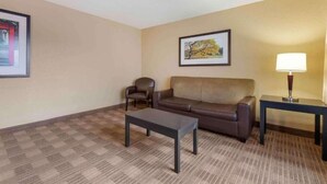 A hotel room with a brown leather sofa, a small armchair, a coffee table, a framed picture on the wall, and a lamp on a side table. - 1 King Bed | Non-Smoking, Kitchen, Shower (Minneapolis MN)