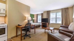 A hotel room with a bed, a desk with a chair, a television, a sofa, and a kitchenette with a stove. - 1 Queen Bed | Non-Smoking, Kitchen, Sofa-Bed (Jackson)