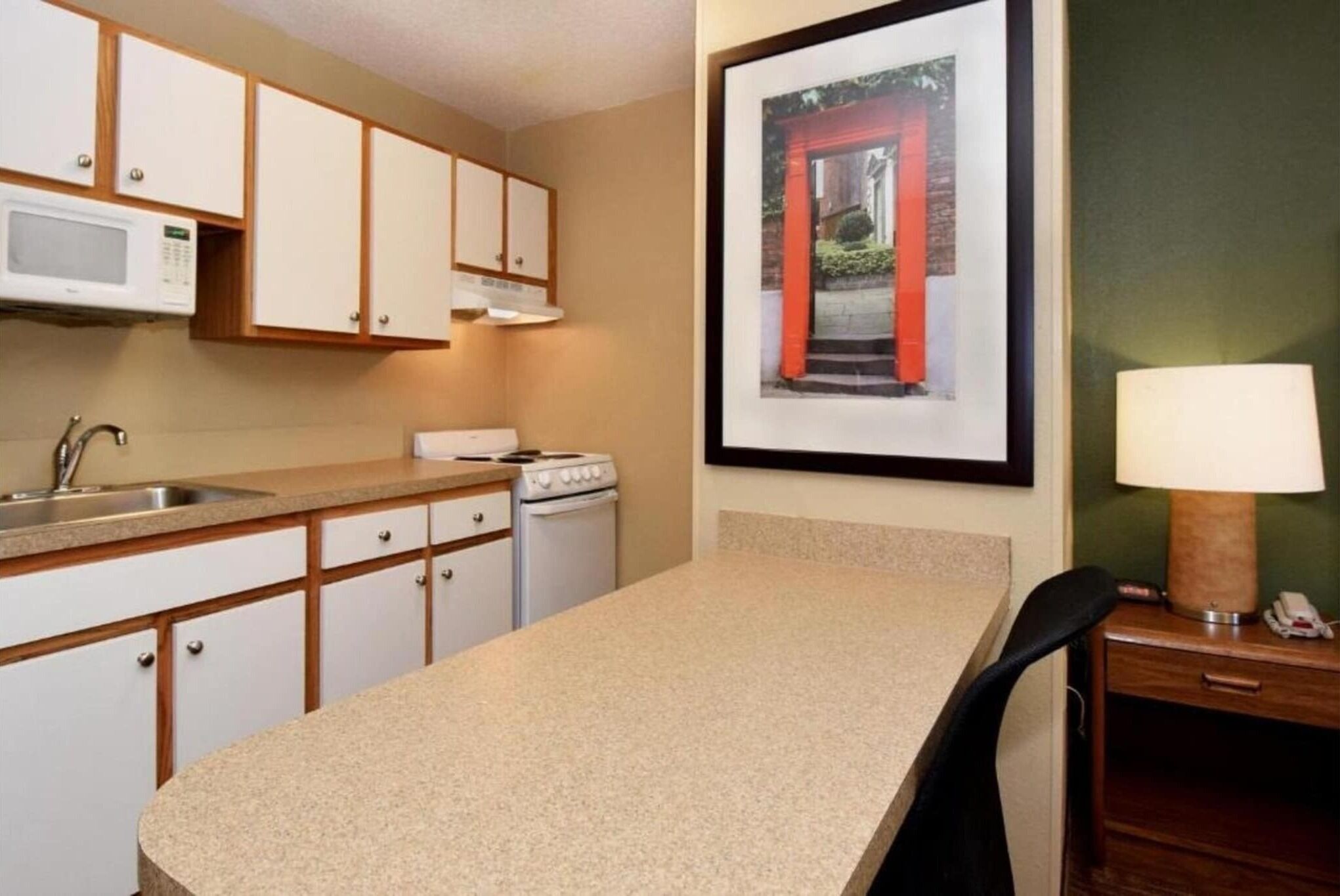 A kitchen with white cabinets, a microwave, a stove, a sink, and a framed picture on the wall.