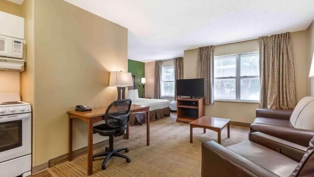 Ein Hotelzimmer mit Bett, Schreibtisch mit Stuhl, Fernseher, Sofa und einer Küchenzeile mit Herd.