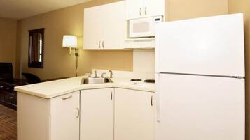 A compact hotel kitchen with white cabinets, a microwave, a sink, and a refrigerator.