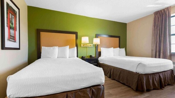 A hotel room with two beds, green walls, and a window with curtains.